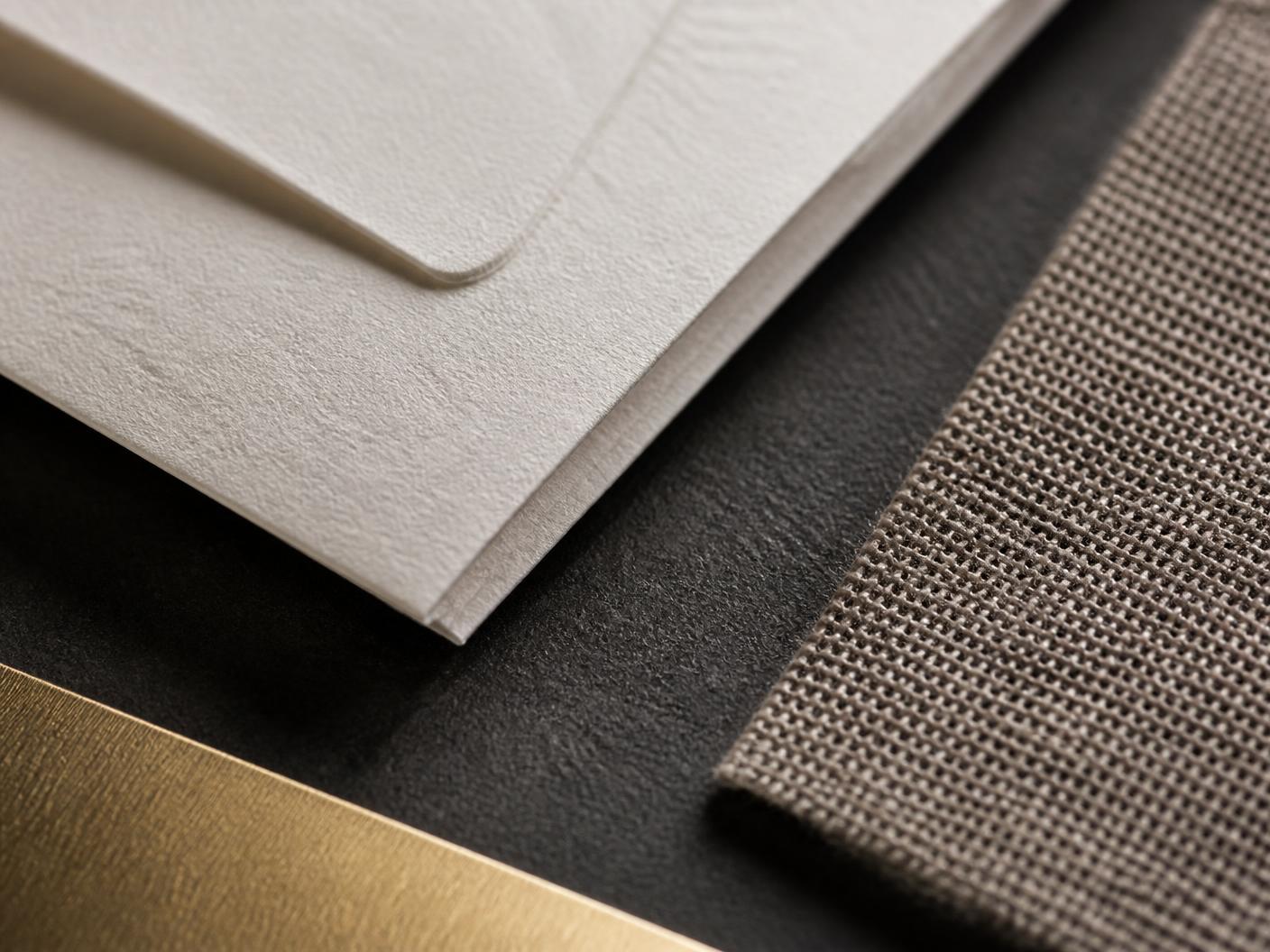 Folded fabric swatches and an embossed ivory card resting on a stone surface.